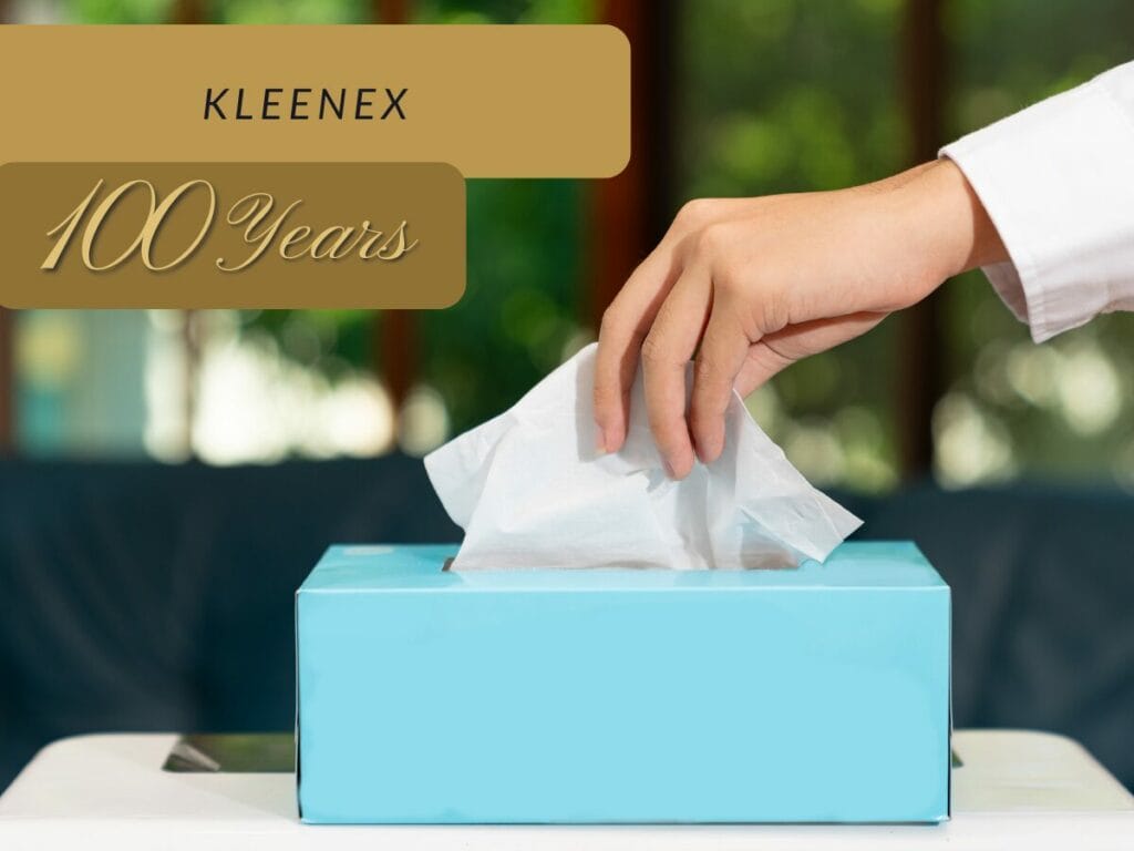 a hand reaching into a box of tissues with the text ‘kleenex 100 years’ above it.