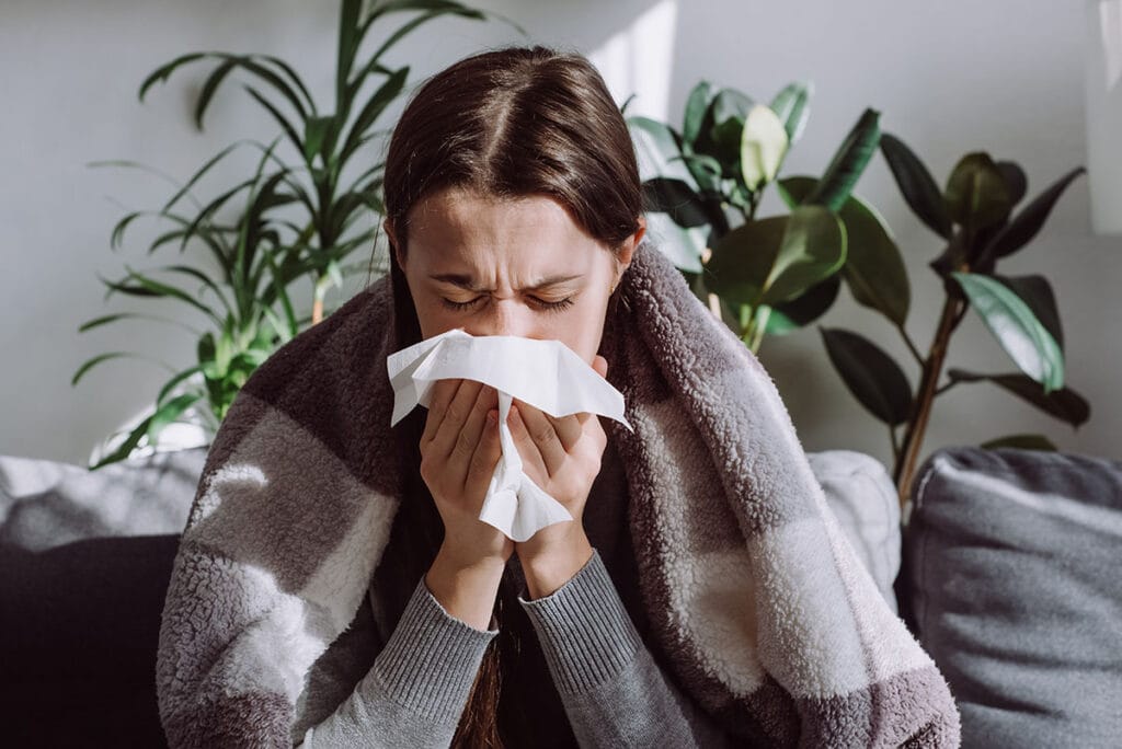woman with the flu sneezing into a kleenex tissue