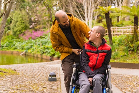 Man in wheelchair smiling, looking up at his friend.