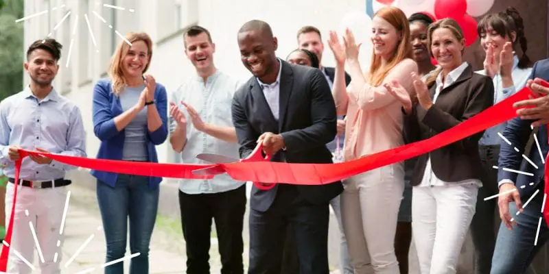Business owner using ribbon cutting tools including a ceremony banner and unique large scissors